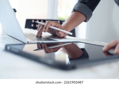 Closeup of business man hand with stylus pen typing on laptop computer and using digital tablet pc on table at home office. Designer working on design project, work from home, paperless office - Powered by Shutterstock