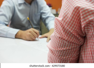 Close-up Of Business Meeting, Two Businessmen Discussing A Deal, Signing A Contract On White Table, With Close Up Waiting Person And The Far Blurred Decision-makers Person In The Orange Wall Painted