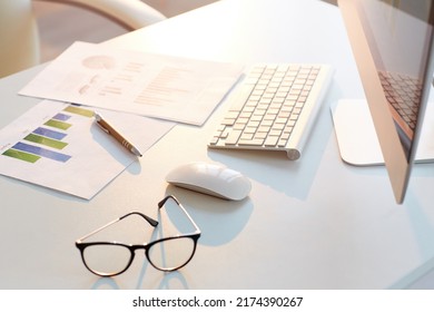 Close-up of business papers with graphs and charts placed on desk with computer, eyeglasses and pen, background