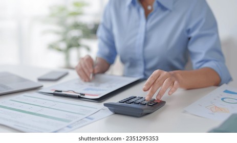 Close-up of business woman hand using a calculator and take notes to check company finances and earnings and budget. - Powered by Shutterstock