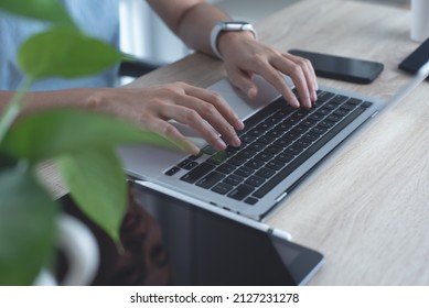 Closeup of business woman working on laptop computer, surfing the internet with mobile phone, digital tablet on table. Young female freelancer with wearing smartwatch online working from home - Powered by Shutterstock