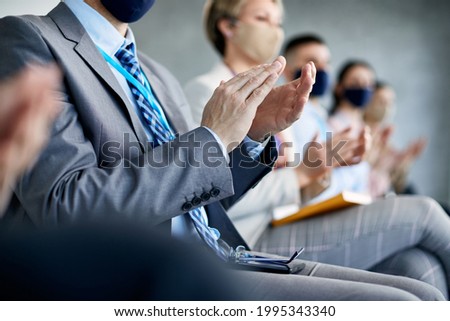 Close-up of businessman clapping hands while attending a seminar with his colleagues during coronavirus pandemic. 