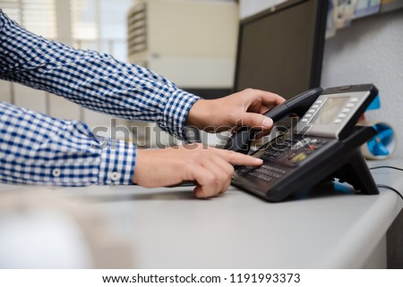Closeup of businessman dialing making office phonecall, light table background. Corporate male holding telephone handle digital electronic pc connection checking daily data news, online chat talk job