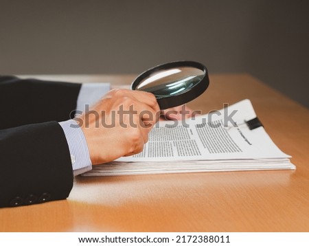 Close-up of businessman hand holding a magnifying glass looking through documents while sitting in the office. Business and learning concept