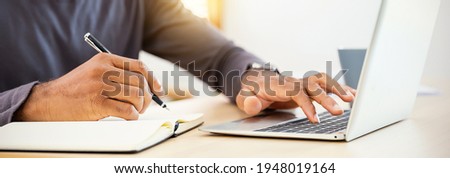 Closeup businessman hand holding pen writing on notebook, work on laptop computer in modern office. Student lecturing while studying online internet course. Write on journal diary panoramic banner