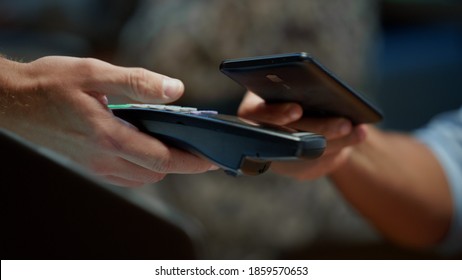 Closeup businessman hand paying with mobile phone over pos terminal with NFC technology. Unrecognizable man using smartphone for wireless money transfer. Unknown customer paying bill in cafe.
