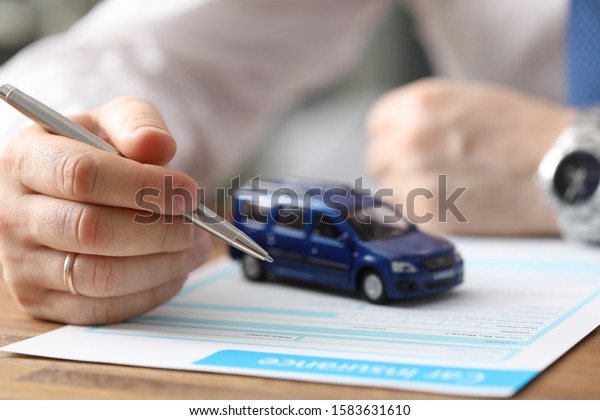 Close-up of businessman hand reading car\
insurance and getting ready to sign. Small blue automobile model on\
wooden table. Protection and business\
concept