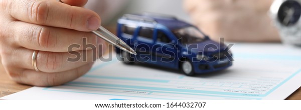 Close-up of businessman hand reading car\
insurance and getting ready to sign. Small blue automobile model on\
wooden table. Protection and business\
concept