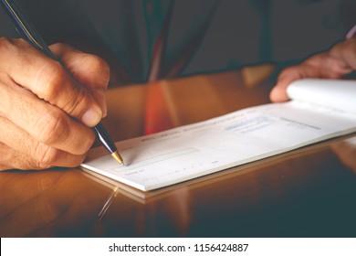 Closeup of businessman hand writing and signing checkbook on the table at office. Business payment by cheque concept. 