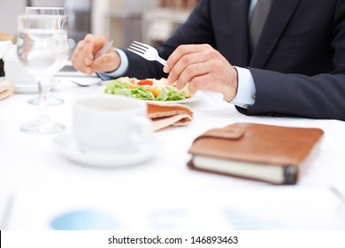 Close-up of businessman hands holding knife and fork over vegetable salad during business lunch