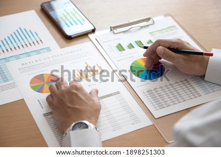 Closeup of businessman hands holding a pencil while reviewing financial statements for business performance or return on investment, ROI analysis. 