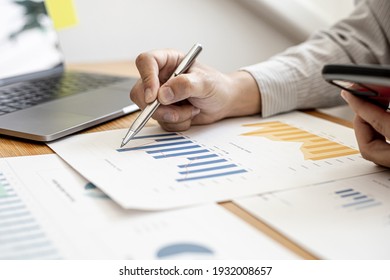 Close-up businessman holding a pen and pointing at a bar chart on a company financial document, he is analyzing historical financial data to plan how to grow the company. Financial concept. - Shutterstock ID 1932008657