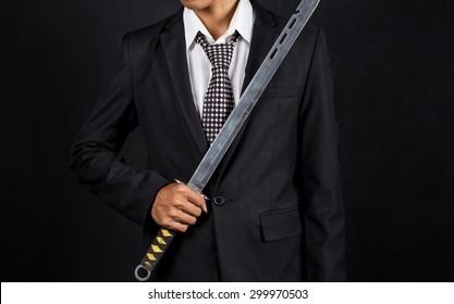 Close-up Of A Businessman Holding Sword Over Black Background