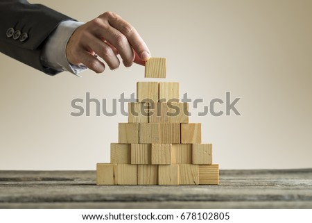 Closeup of businessman making a pyramid with empty wooden cubes. Concept of business hierarchy.