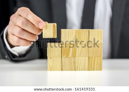 Closeup of businessman making a structure with wooden cubes. Building a business concept.
