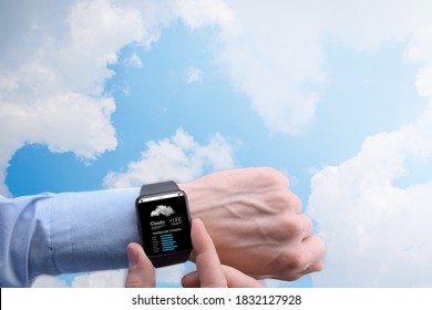 Close-up Of A Businessman Man Male Checking Weather On Smartwatch App Program On A Background Of Blue Sky With White Clouds.