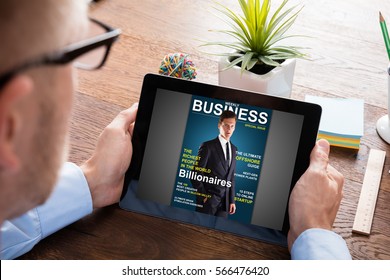 Close-up Of A Businessman Reading Online Magazine On Digital Tablet At Wooden Desk