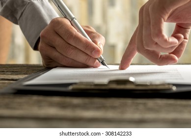 Closeup of businessman showing his new business partner where to sign an agreement or contract with fountain pen  on rustic wooden desk. 