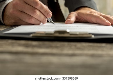 Closeup Of Businessman Signing Contract, Document Or Legal Papers Clipped On Clipboard With Fountain Pen.