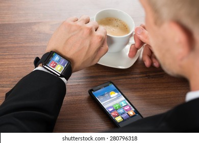 Close-up Of Businessman With Smartphone And Smartwatch Holding Cup Of Coffee On Desk - Powered by Shutterstock