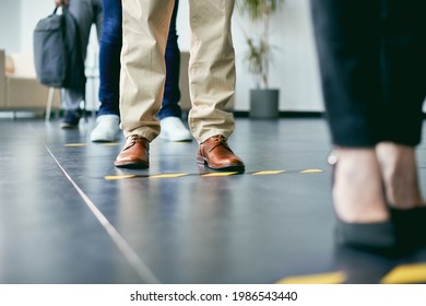 Close-up of businessman standing behind social distancing line while waiting with group of coworkers at office building hallway. 
