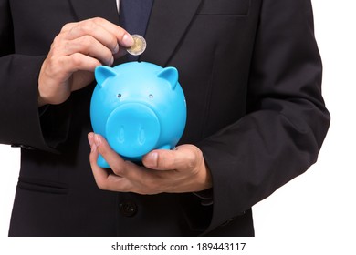Closeup of businessman in a suit standing holding a blue piggy bank.