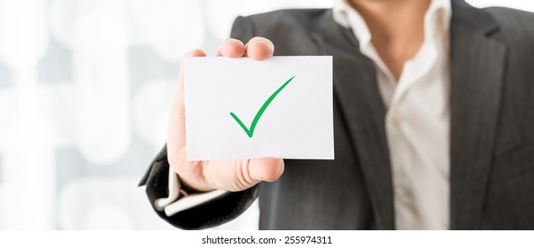 Closeup of businessman or teacher holding up a white card with green check mark. Conceptual of successfully completed task or homework. - Shutterstock ID 255974311