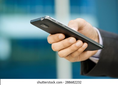 Closeup of businessman typing note on mobile phone. The man writes on his smartphone using one hand with office building in background. 