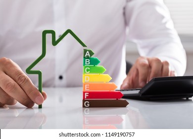 Close-up of a businessman using calculator holding outline of house model with energy efficiency rate - Powered by Shutterstock