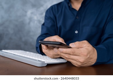 Close-up of a businessman using smartphone with keyboard on desk, representing digital communication, online work, mobile connectivity, technology usage, and business productivity in modern life.