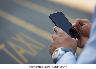 Closeup Of Businessman Using Smartphone On Street To Call A Taxi Cab. Detail Of  Black Hand Holding Mobile Phone While Using High Speed Internet Connection. Closeup Of Empty Screen Of Cellphone.