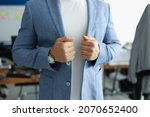 Close-up of businessman wearing stylish costume and corrects jacket with hand. Well-dressed man posing in personal office. Presentable look at work. Business and job concept