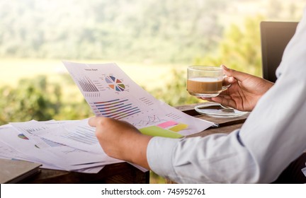 Close-up businessman working on wooden desk and holding graph documents with coffee cup