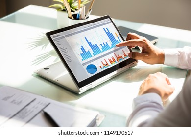 Close-up of a businessman's hand analyzing graph on laptop at workplace