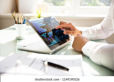 Close-up of a businessman's hand analyzing graph on laptop at workplace