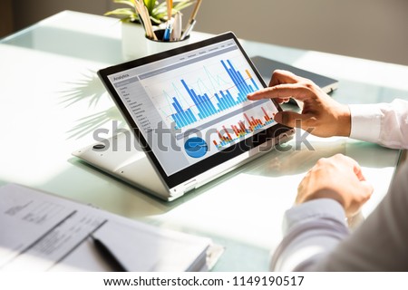 Close-up of a businessman's hand analyzing graph on laptop at workplace