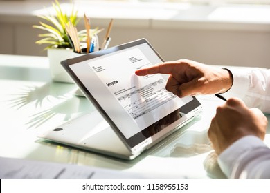 Close-up of a businessman's hand examining invoice on laptop