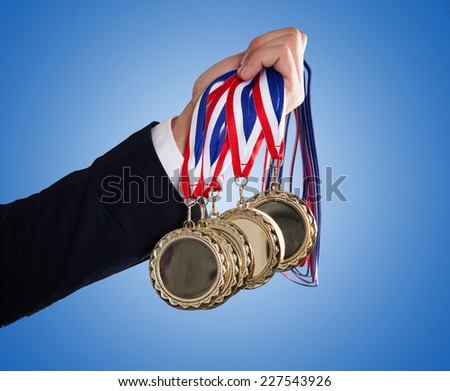 Closeup of businessman's hand holding medals over blue background