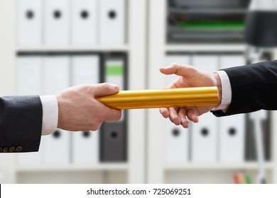 Close-up Of Businessman's Hand Passing Golden Relay Baton To His Colleague In Office - Shutterstock ID 725069251