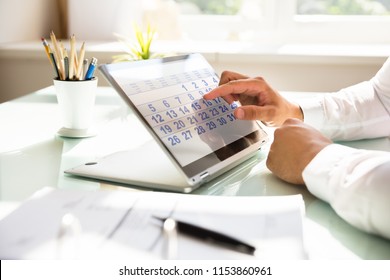 Close-up of a businessman's hand using calendar on laptop over desk