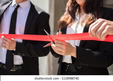 Close-up Of Businesspeople Hand Cutting Red Ribbon With Scissors