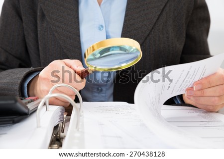 Close-up Of Businessperson Checking Bills With Magnifying Glass