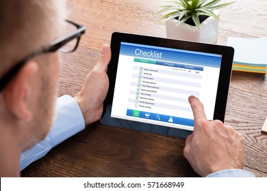 Close-up Of A Businessperson Filling Checklist Form On Digital Tablet At Wooden Desk