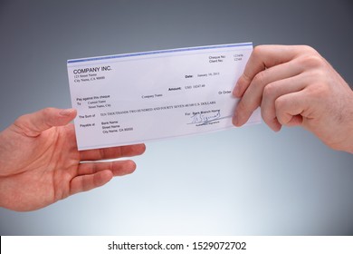 Close-up Of A Businessperson Giving Cheque To Colleague On Grey Background