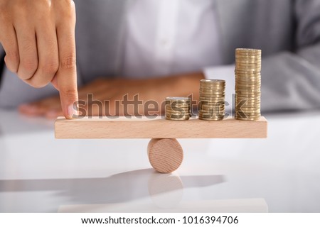 Close-up Of Businessperson's Finger Balancing Stacked Of Coins On Wooden Seesaw