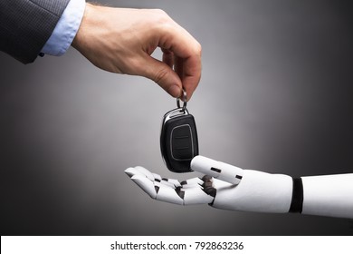 Close-up Of A Businessperson's Hand Giving Car Key To Robot On Grey Background