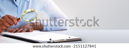 Close-up Of A Businessperson's Hand Looking At Contract Form Through Magnifying Glass