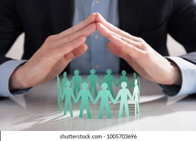 Close-up Of A Businessperson's Hand Protecting Blue Paper Cut Out Figures On White Background - Powered by Shutterstock