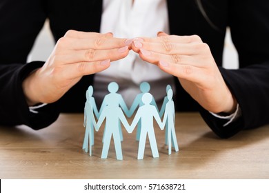 Close-up Of Businesswoman Hand Protecting Cut-out Figures On Desk In Office - Powered by Shutterstock