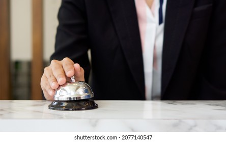 Closeup of a businesswoman hand ringing silver service bell on hotel reception desk.